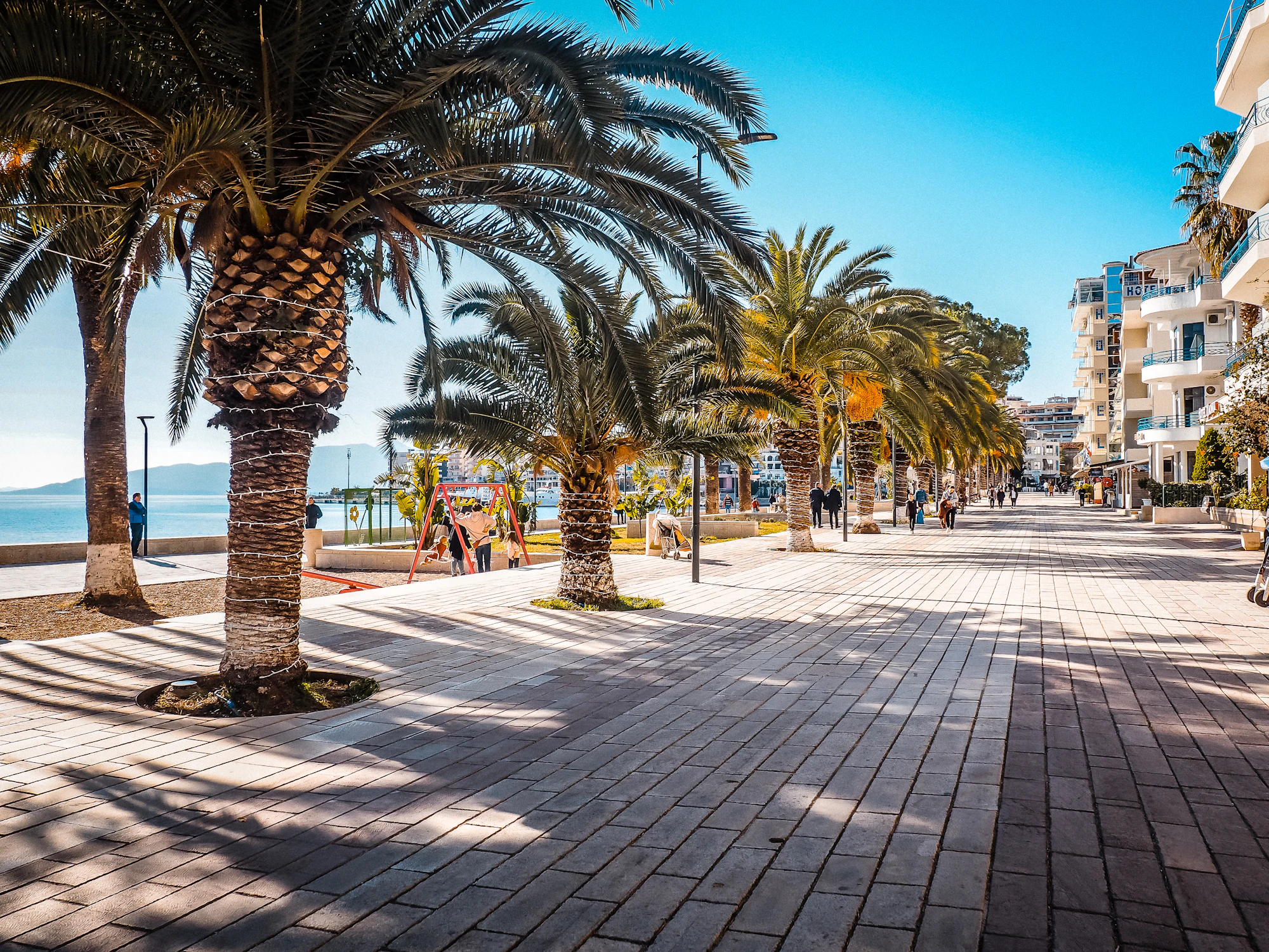 Saranda (Sarandë) Lungomare promenade — A palm tree lined street next to the ocean